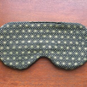 Op de afbeelding: Een zwart slaapmasker met een gouden geometrisch patroon. Het masker is gemaakt van zacht materiaal en is ontworpen om licht te blokkeren.