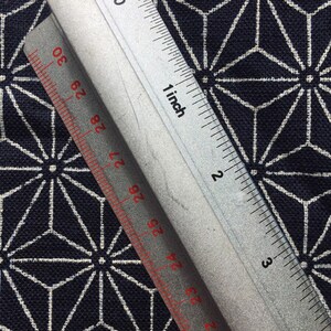 Op de afbeelding: Een zilveren liniaal met rode markeringen, die tot 4 inch meet, ligt op een donkerblauwe stof met een wit geometrisch patroon.