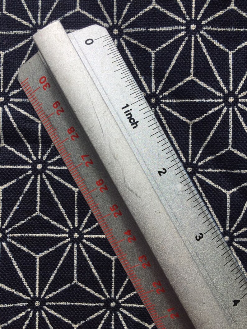 Op de afbeelding: Een zilveren liniaal met rode markeringen, die tot 4 inch meet, ligt op een donkerblauwe stof met een wit geometrisch patroon.