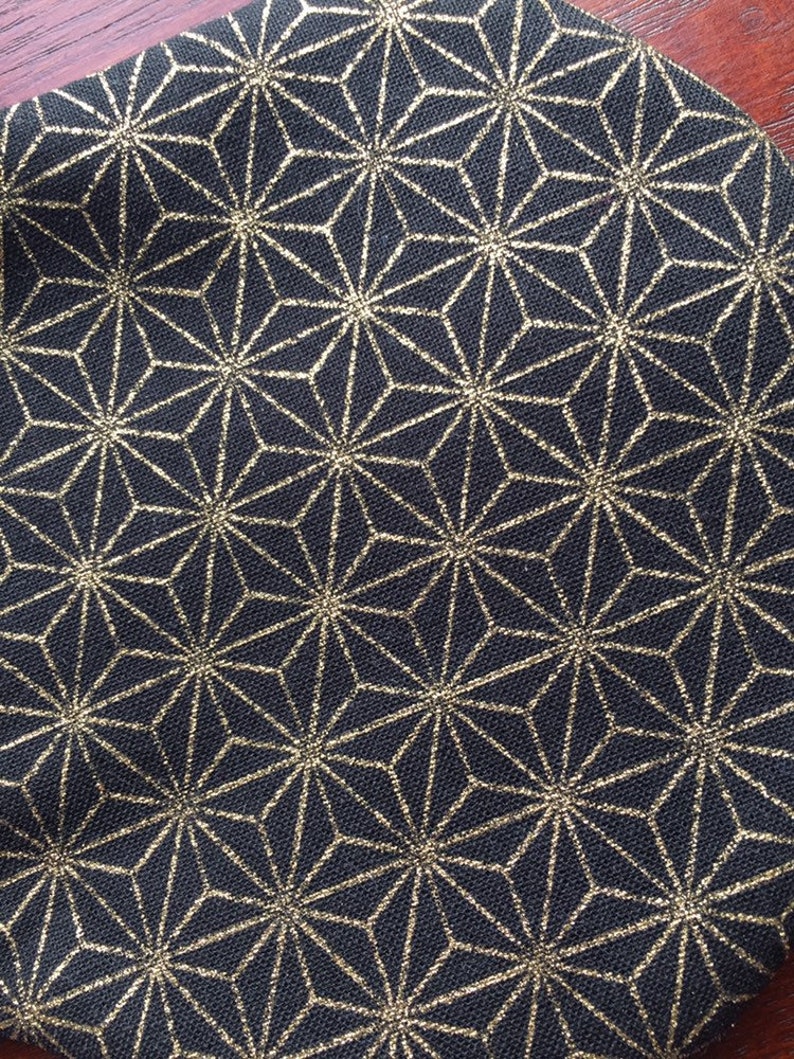 Op de afbeelding: Zwarte stof met een gouden geometrisch patroon. Het patroon bestaat uit herhalende sterren.