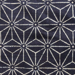 Op de afbeelding: Een donkerblauwe stof met een wit geometrisch patroon van herhalende sterren. De stof heeft een textuur van geweven materiaal.