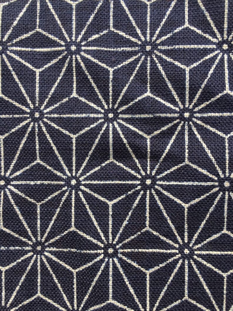 Op de afbeelding: Een donkerblauwe stof met een wit geometrisch patroon van herhalende sterren. De stof heeft een textuur van geweven materiaal.