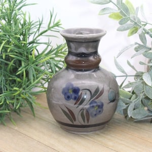 May include: A small, gray ceramic vase with a brown band around the neck. The vase is decorated with blue and green floral designs.
