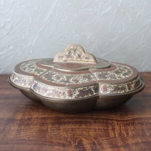 May include: A decorative brass serving dish with a floral design in shades of gold, red, and white. The dish has a lid with a decorative handle.