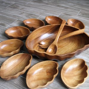 May include: A set of wooden serving bowls, including a large, scalloped bowl and several smaller bowls. The bowls are made of natural wood and have a warm, rustic look. The set also includes two wooden serving spoons.