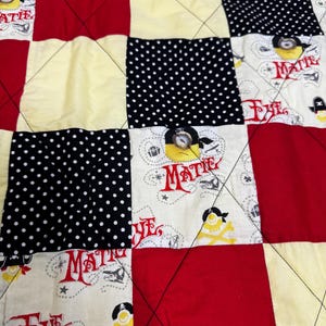 May include: A patchwork quilt featuring a repeating pattern of red, cream, and black-and-white polka dot fabric squares. The cream squares display a pirate-themed print with yellow cartoon characters, anchors, and the red text "MATIE".
