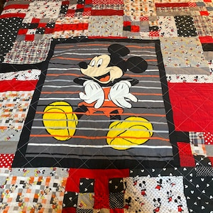 May include: A red, black and grey patchwork quilt with a large Mickey Mouse image in the centre. The quilt features a variety of Mickey Mouse patterns.