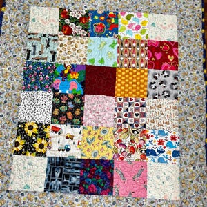 May include: A patchwork quilt featuring a variety of colorful fabric squares with diverse patterns including sunflowers, cartoon characters, animals, hearts, and geometric shapes, all bordered by a light gray fabric with a repeating teddy bear print.
