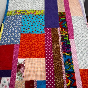 May include: A patchwork quilt featuring a variety of fabric patterns including floral prints, polka dots, animal print, gingham, and a top border with black and white cat illustrations. The quilt is constructed with rectangular and square panels.