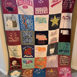 Könnte beinhalten: Eine Decke aus verschiedenen T-Shirts mit den griechischen Buchstaben Alpha Omicron Pi, den Worten "Nebraska Greeks", "Naturally Some Letters" und "Greek Life Found You".