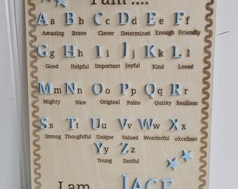 May include: A rectangular wooden wall plaque featuring a light blue ribbon hanger. The board displays the alphabet in light blue letters, each paired with a positive adjective. The text includes 'I am', the name 'JACE', and 'Allah created me in the best way'.
