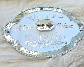 May include: An oval mirrored ring holder tray featuring a white center panel with the names Adam and Salma engraved in script, alongside Arabic calligraphy. The mirrored border is decorated with small white beads and two clear crystal knobs.