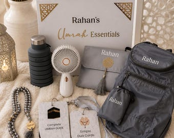 May include: A gift set labeled Rahan's Umrah Essentials containing a dark gray collapsible water bottle, a white handheld fan, a gray pouch with a gold tassel, a gray backpack, prayer beads with a gold charm, and two cards labeled Complete UMRAH GUIDE and Simple Dua Cards.