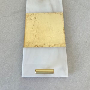 May include: A white marble serving tray with gold leaf accents and two gold metal handles.