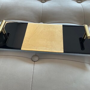 May include: A black and gold rectangular serving tray with two gold handles. The tray has a black border and a gold center section.