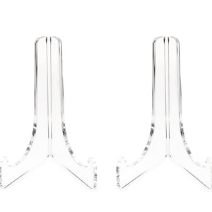 May include: Two clear acrylic display stands for showcasing items like plates, photos, or artwork. Each stand has a triangular base and a curved, angled top.