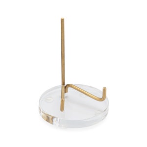 May include: A clear acrylic display stand with a gold metal easel. The stand has a round base and a single upright support.