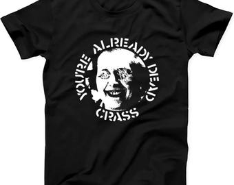 May include: A black short-sleeve t-shirt featuring a white circular graphic on the chest. The graphic depicts a smiling face with distorted eyes, surrounded by the text "YOU'RE ALREADY DEAD" at the top and "CRASS" at the bottom in a bold font.