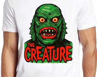 May include: White t-shirt featuring a green monster graphic with red eyes, mouth, and the text "THE CREATURE" in red. The design is a vintage-style illustration, perfect for fans of classic horror.