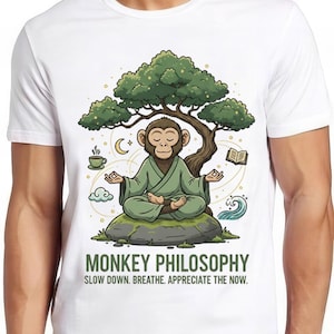 May include: White t-shirt featuring a cartoon monkey meditating under a tree. The monkey is wearing a green robe and sitting on a rock. The shirt has the text "MONKEY PHILOSOPHY" and "SLOW DOWN. BREATHE. APPRECIATE THE NOW."