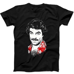 Peut inclure: Un t-shirt noir à manches courtes arborant une illustration graphique blanche à fort contraste représentant un homme avec une moustache et des cheveux bouclés. Il porte une chemise rouge à motif floral blanc au niveau du col.