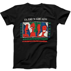 May include: A black short-sleeved t-shirt featuring the text TALKING HEADS in white above a rectangular graphic. The graphic displays four stylised red figures against a background of blue, green, and white shapes, with additional coloured lines and triangles.