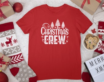 Puede incluir: Camiseta roja con texto blanco que dice "Christmas Crew" y un gráfico de un gorro de Papá Noel, árboles de Navidad y luces.