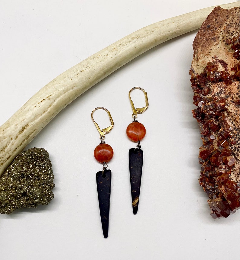 May include: A pair of earrings with a black, pointed, wood-like pendant and a round, orange stone bead.