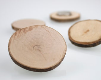 May include: Four small, round wooden coasters with natural wood grain and bark edges are scattered on a white surface. The coasters are light brown with visible growth rings, showcasing a rustic aesthetic. The focus is on the texture and organic design.
