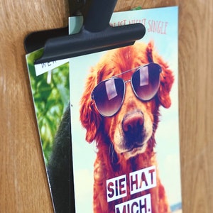 May include: A card featuring a golden retriever wearing sunglasses. The text on the card reads "Sie hat mich."