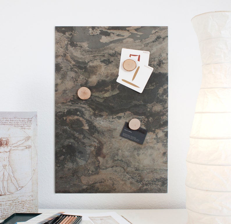 May include: A magnetic slate board with a dark gray and brown marbled pattern. Three wooden round magnets are attached to the board, holding a business card and two pieces of paper.