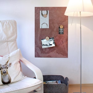 May include: A red-brown magnetic board with a variety of items pinned to it using wooden round magnets. The items include a photo, a card with text, and a business card. The board is mounted on a white wall.