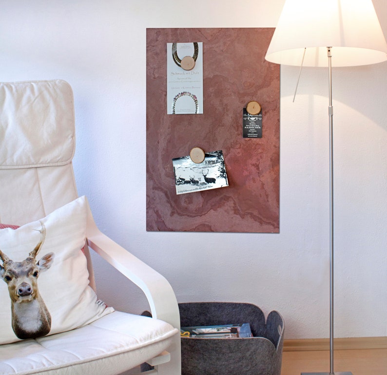 May include: A red-brown magnetic board with a variety of items pinned to it using wooden round magnets. The items include a photo, a card with text, and a business card. The board is mounted on a white wall.