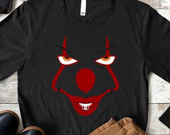 May include: Black t-shirt with a red and white clown face graphic. The graphic features a red nose, white teeth, and red and white eyes.