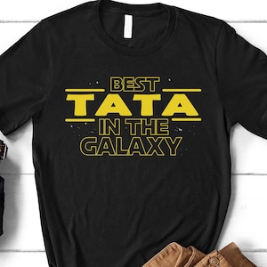 May include: Black t-shirt with yellow text that reads "Best Tata in the Galaxy".