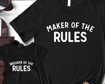 Może przedstawiać: Dwie czarne koszulki z białym nadrukiem. Większa koszulka z napisem "Maker of the Rules". Mniejsza koszulka z napisem "Breaker of the Rules".