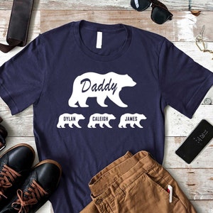 K&ouml;nnte beinhalten: Ein marineblaues T-Shirt mit einer wei&szlig;en B&auml;rensilhouette und dem Text "Daddy" dar&uuml;ber. Drei kleinere B&auml;rensilhouetten befinden sich unter dem gro&szlig;en B&auml;ren mit den Namen "Dylan", "Caleigh" und "James" darunter.
