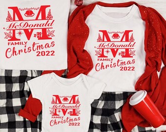 May include: A set of four white Christmas pajamas with red and black plaid pants. The shirts feature a red monogram with the text "McDonald Family Christmas 2022".