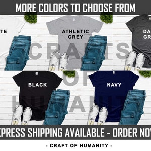May include: Six t-shirts laid out on a white wood surface, showing different color options. The colors are white, athletic grey, dark grey, black, navy, and a light blue. The text "MORE COLORS TO CHOOSE FROM" is at the top of the image. The text "CRAFT OF HUMANITY" is at the bottom of the image.