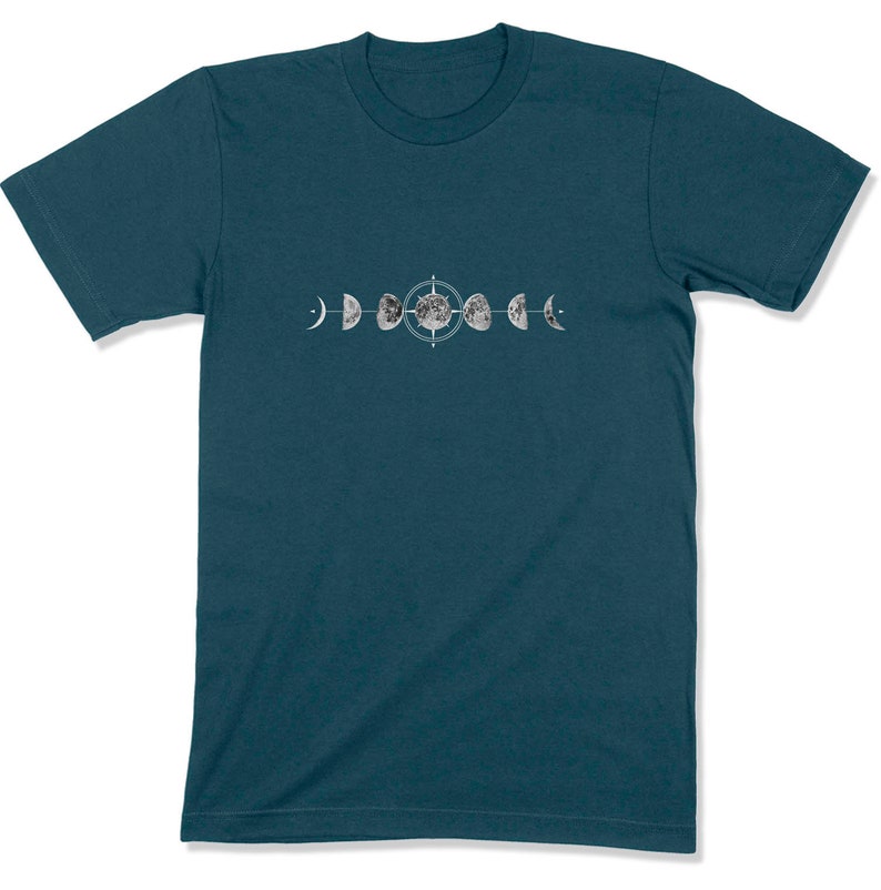 May include: A teal blue t-shirt with a white graphic of the moon in different phases. The graphic includes a compass symbol in the center.