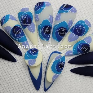 Pu&ograve; includere: Un set di dieci unghie finte lunghe a forma di mandorla con un design floreale blu e bianco. Alcune unghie sono di un blu navy solido, mentre altre presentano una base bianca con rose blu e foglie.