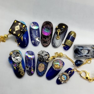 May include: Ten blue and gold nail charms with different designs, including a book, a moon, a crystal, a face, and a globe. The charms are attached to gold chains.