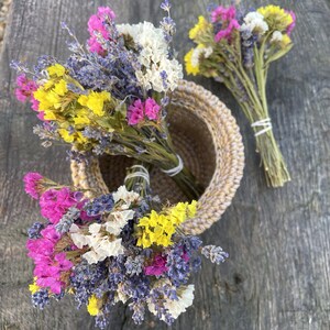 May include: A bouquet of dried flowers in shades of purple, yellow, and pink, arranged in a woven basket. The flowers include lavender, statice, and baby's breath.