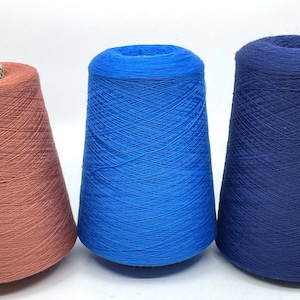 May include: Three cones of yarn in different colours: coral, blue, and navy blue. The cones are cone-shaped and made of a soft, textured material.