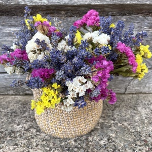 May include: A bouquet of dried flowers in a woven basket. The flowers are purple, pink, white, and yellow.