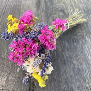 May include: A bouquet of dried flowers in shades of pink, purple, and yellow. The flowers are tied together with a brown ribbon.