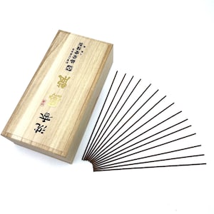 Può includere: Una scatola di legno con testo giapponese sul coperchio, contenente un mazzo di bastoncini di incenso marroni. Il testo sulla scatola recita "宝仙堂  特撰  沈香  香  -  宝仙堂  特撰  沈香  香  -  宝仙堂  特撰  沈香  香".