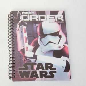May include: A black and white spiral notebook with a Star Wars themed cover featuring a First Order Stormtrooper with the text "First Order Executioner" and "Star Wars".