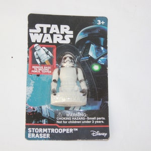 May include: A white plastic Star Wars Stormtrooper eraser with a black base. The eraser can be removed to become a pencil topper. The packaging features a warning for choking hazards and is labeled for ages 3 and up.