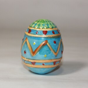 May include: A blue and yellow ceramic Easter egg with red and green accents. The egg is decorated with a geometric pattern.